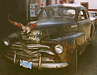 [Old sedan with steer horns tied onto the hood parked in front of the Alamos town market: 38k]