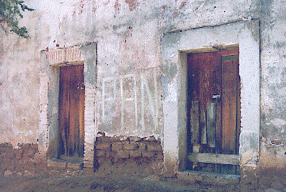 [Stuccoed wall with old wooden entry doors and the weathered adobe block showing at the base: 51k]
