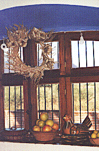 [La Puerta Roja blue framed dining room window, a corn husk wreath, Mexican pottery and fruit with view out to the Alamos mountains: 35k]
